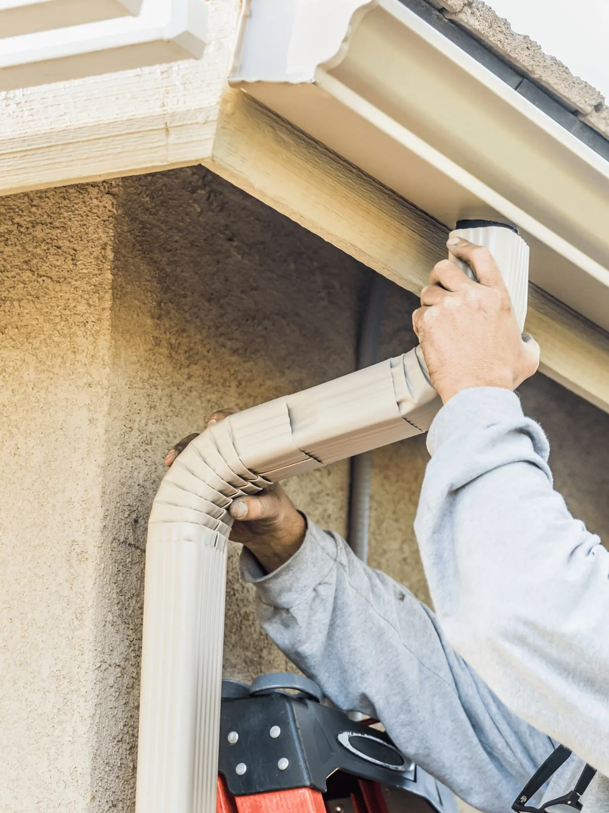 Installer attaching a downspout to a stucco wall