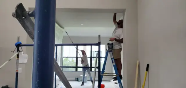 Excell painter working on an interior wall with ladder and drop cloths